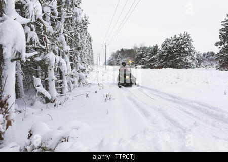 Ansicht der Rückseite des Jugendjungen Quad fahren auf Schnee gegen den Himmel Stockfoto