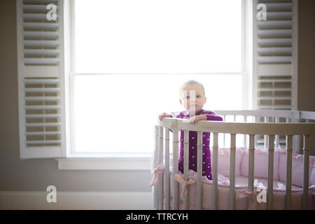 Portrait von niedlichen Baby Mädchen im Kinderbett gegen Fenster zu Hause Stockfoto