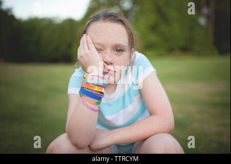 Portrait von gelangweilten Mädchen mit der Hand am Kinn sitzen gegen Bäume im Park Stockfoto