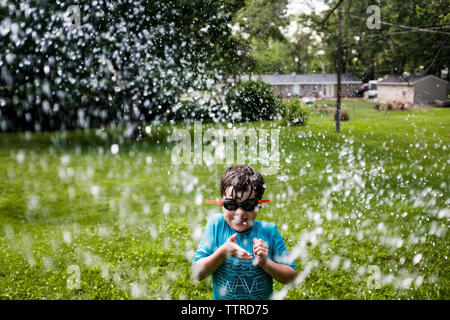 Verspielte junge tragen Schwimmbrille beim Spielen mit Wasser im Hof Stockfoto