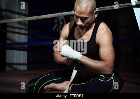 Reifer Mann einwickeln Verband an der Hand während der Sitzung gegen Boxring in der Turnhalle Stockfoto