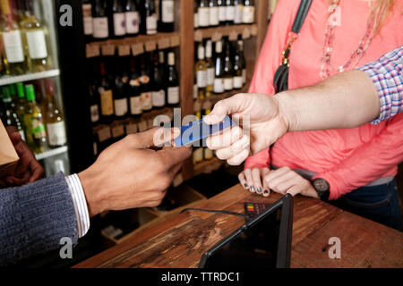 Hohe Betrachtungswinkel und der Inhaber eines kleinen Unternehmens, die Kreditkarte von Kunden an Wein Shop Stockfoto