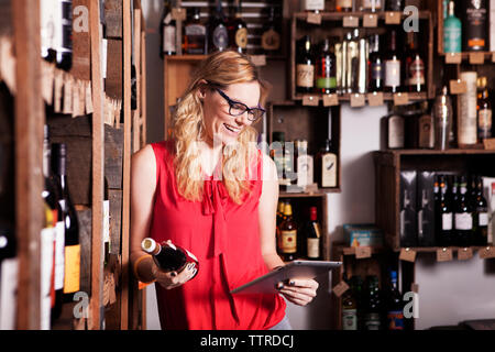 Gerne weibliche Unternehmer mit Tablet Computer halten sie Flasche Wein im Shop Stockfoto