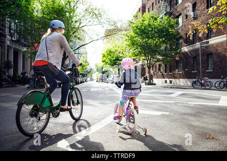 Hintere Ansicht von Mutter und Tochter auf dem Fahrrad über Straße Stockfoto