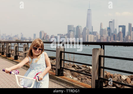 Portrait von Mädchen mit dem Fahrrad auf der Promenade mit Sicht auf die City Skyline im Hintergrund Stockfoto