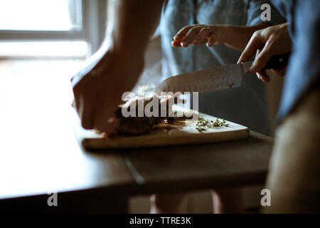Mittelteil der Freunde schneiden gekochtes Lamm am Tisch Stockfoto