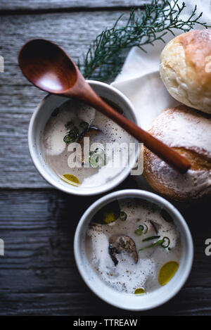 Overhead shot der Pilzsuppe mit Löffel und Brötchen auf hölzernen Tisch Stockfoto