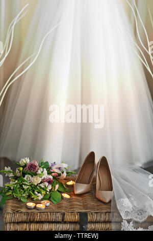 Schuhe auf wicker Brust und Hochzeit Kleid hängen an der Wand im Zimmer Stockfoto