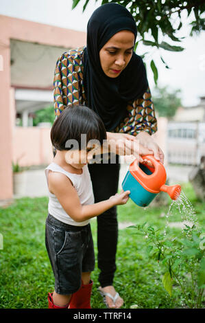 Mutter mit Sohn Bewässerung von Pflanzen im Hinterhof Stockfoto