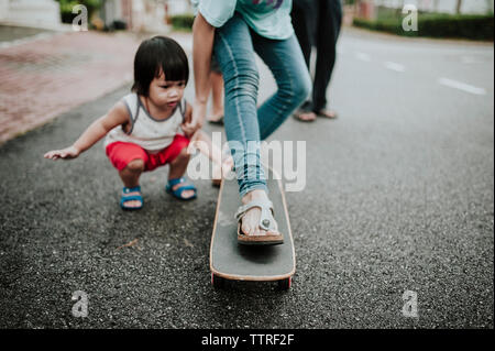 Jungen auf der Suche nach Schwester skateboarding auf der Straße Stockfoto