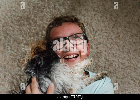 Close-up Happy Boy umarmen Yorkshire Terrier beim Liegen auf dem Teppich zu Hause Stockfoto