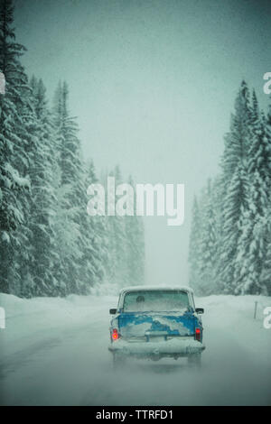 Schnee bedeckt Auto auf der Straße inmitten von Wald im Winter Stockfoto