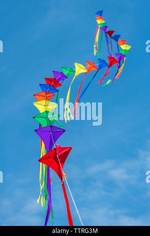 Eine Reihe von bunten Drachen auf einer einzelnen Zeile gegen ein strahlend blauer Himmel. Stockfoto