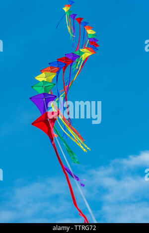 Eine Reihe von bunten Drachen auf einer einzelnen Zeile gegen ein strahlend blauer Himmel. Stockfoto