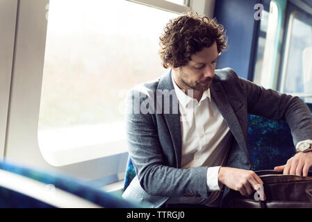 Geschäftsmann, der im Zug sitzt und in der Tasche sucht Stockfoto