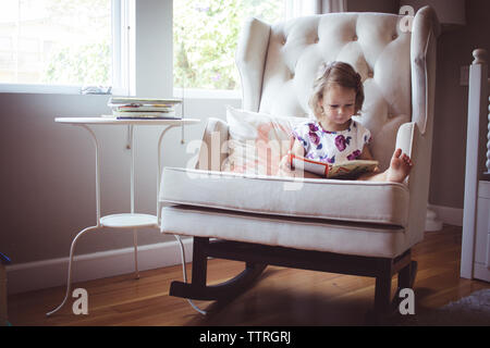 Mädchen lesen Bild Buch während auf Schaukelstuhl zu Hause sitzen Stockfoto