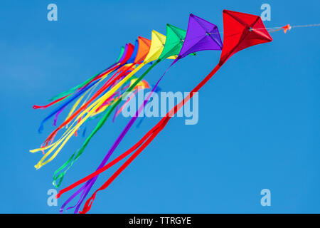 Eine Reihe von bunten Drachen auf einer einzelnen Zeile gegen ein strahlend blauer Himmel. Stockfoto