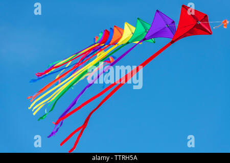 Eine Reihe von bunten Drachen auf einer einzelnen Zeile gegen ein strahlend blauer Himmel. Stockfoto