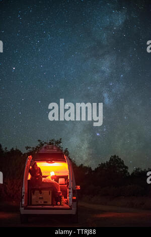 Mann sitzt in beleuchteten Wohnmobil gegen star Feld in der Nacht Stockfoto