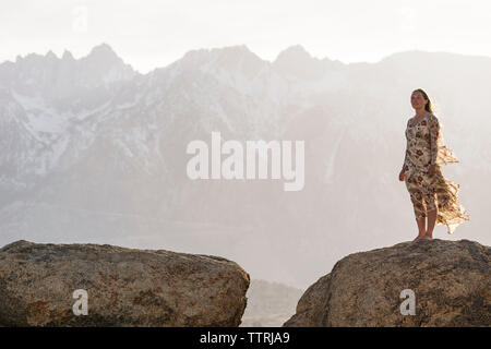 Junge Frau steht auf Rock gegen Berge bei nebligen Wetter Stockfoto