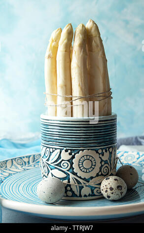 Spargel mit Wachteleier in der Platte auf dem Tisch gegen blaue Wand Stockfoto