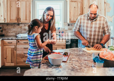 Die Eltern Essen zubereiten, während mit Tochter in der Küche zu Hause stehend Stockfoto