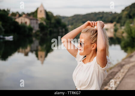 Lächelnde Frau binden Haar, während durch die Saone Fluss gegen Himmel stehen bei Sonnenuntergang Stockfoto