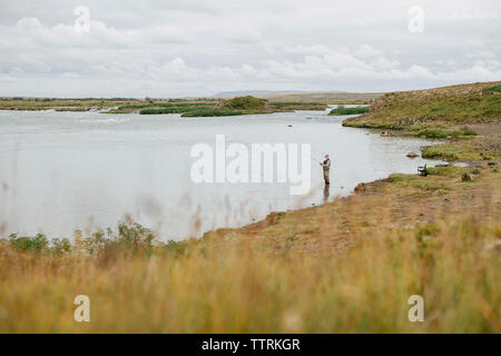 Hohe Betrachtungswinkel von Mann angeln beim Stehen in der See gegen bewölkter Himmel Stockfoto