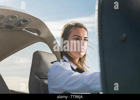 Low Angle View der weiblichen Pilot-Bedienfeld beim Sitzen im Flugzeug gegen den blauen Himmel am Flughafen Stockfoto