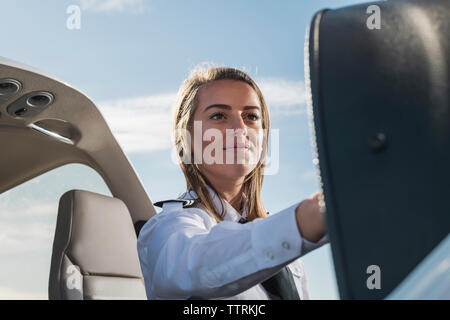 Low Angle View von lächelnd weibliche Pilot-Systemsteuerung im Flugzeugmodus gegen den blauen Himmel sitzt am Flughafen Stockfoto