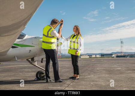 Seitenansicht der männlichen Ingenieur, Flugzeugteile für die weiblichen Auszubildenden beim Stehen vor blauem Himmel auf der Landebahn Stockfoto