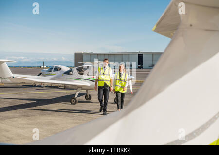 Männliche Ingenieur mit weiblichen Auszubildenden wandern gegen den blauen Himmel auf Landebahn während der sonnigen Tag Stockfoto