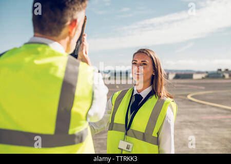 Ansicht der Rückseite des männlichen Ingenieur, Flugzeugteile für die weiblichen Auszubildenden beim Stehen vor blauem Himmel auf der Landebahn Stockfoto