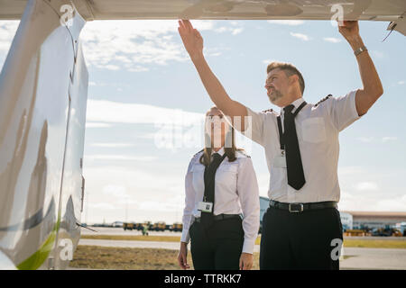 Low Angle View männlichen Ingenieur, Flugzeugteile für die weiblichen Auszubildenden während gegen den blauen Himmel stehen auf Landebahn während der sonnigen Tag Stockfoto