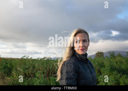 Attraktive nachdenklich blonde Frau weg zwischen Wilde Lande mit grünen Büschen in der Nähe von Bergen und bewölkter Himmel suchen Stockfoto