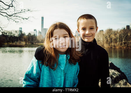 Portrait von lächelnden Bruder mit Arm um Schwester am See im Park Stockfoto