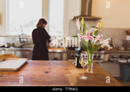 Wineglass durch die Vase auf dem Tisch mit Frau im Hintergrund arbeiten zu Hause Stockfoto