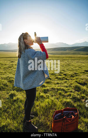 Seitenansicht der weiblichen Wanderer Trinkwasser beim Stehen auf Wiese gegen den klaren Himmel Stockfoto