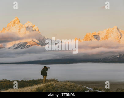 Seitenansicht der Wanderer das Fotografieren mit der Kamera beim Stehen gegen Berge Stockfoto