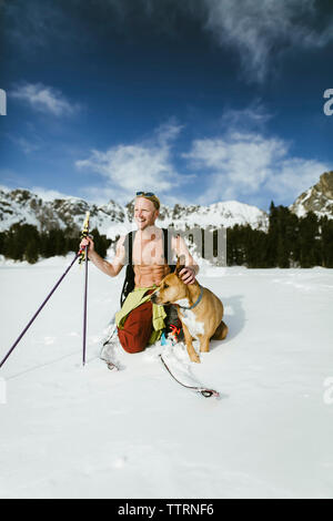 Fröhliche Wanderer mit Hund auf schneebedeckten Feld gegen Berge Stockfoto