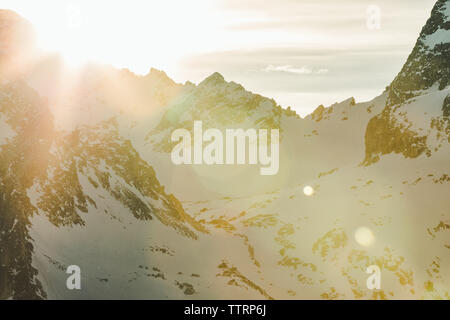 Schneebedeckte Berge und Sonne flare bei Sonnenuntergang auf schroffen Ridgeline Stockfoto