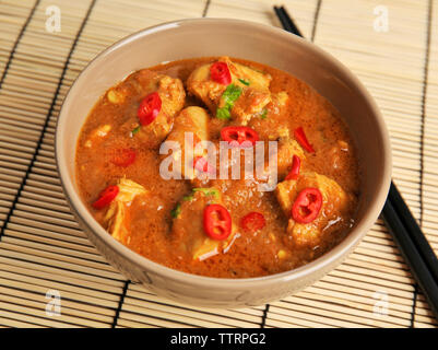 Leckere Chicken Curry in der Schüssel und Essstäbchen auf Bambus Matte Stockfoto