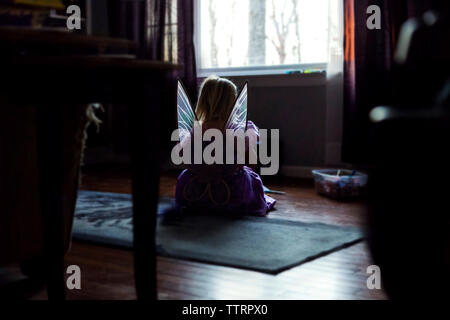 Ansicht der Rückseite des Mädchens in Fee Kostüm auf dem Boden zu Hause sitzen Stockfoto