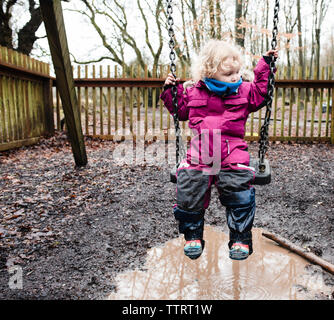 Volle Länge des Mädchen sitzen auf Swing im Park während der Regenzeit Stockfoto