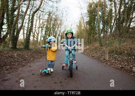 Portrait von Geschwister reiten push Roller und Fahrrad auf der Straße gegen den Himmel Stockfoto