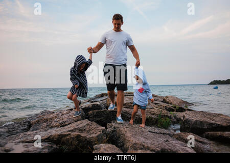 Vater und Kinder zu Fuß auf den Felsen, vom Meer gegen Sky Stockfoto