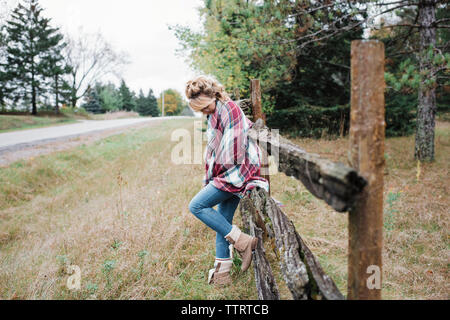 Die ganze Länge der nachdenkliche Frau, die gegen Holzzaun in das Feld Stockfoto