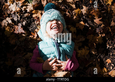 Hohe Betrachtungswinkel von nettes Mädchen mit Hände auf Bauch lachen während auf gefallene Blätter im Herbst liegen Stockfoto