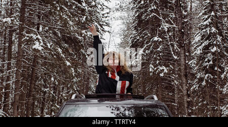 Verspielte Frau mit Arm angehoben blasen Bubble Gum beim Stehen in dem Auto im Winter Stockfoto