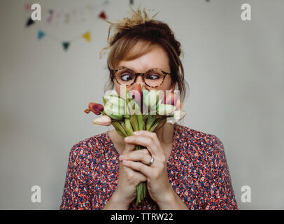 In der Nähe von Frau riechen Tulpen, während das Gesicht gegen die Wand zu Hause Stockfoto